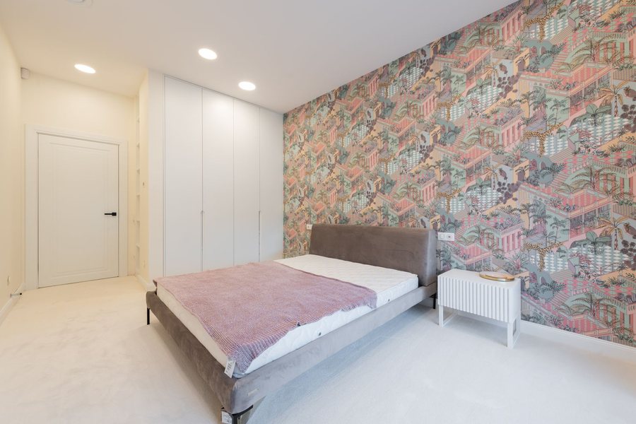 Bright bedroom with a scenic patterned accent wall beside a white wardrobe