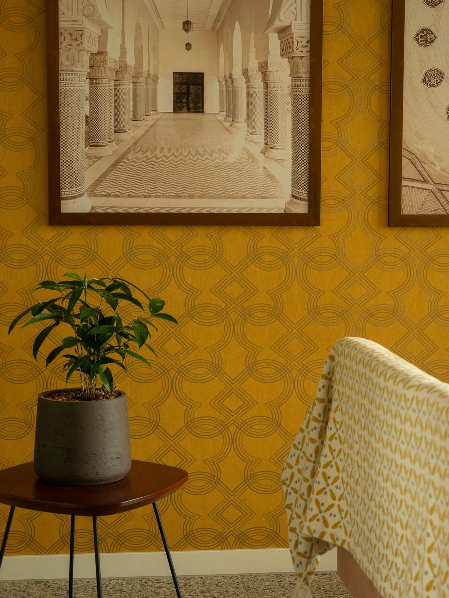 Seating nook with a warm yellow patterned wall, plant and rattan chair