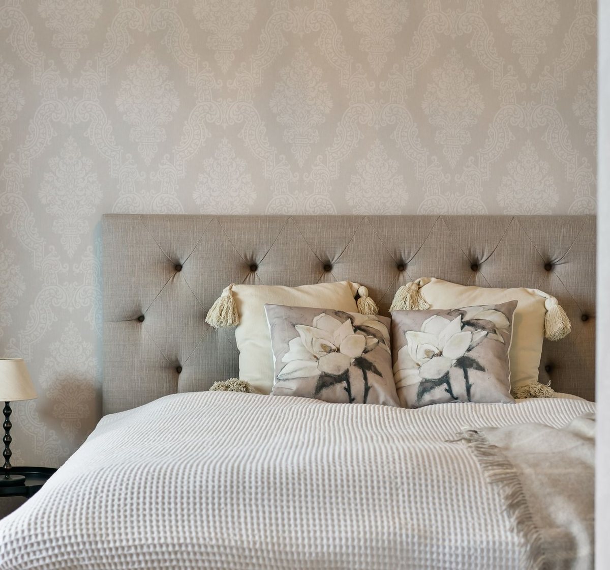 Neutral bedroom with a subtle tone-on-tone damask wallpaper behind an upholstered bed