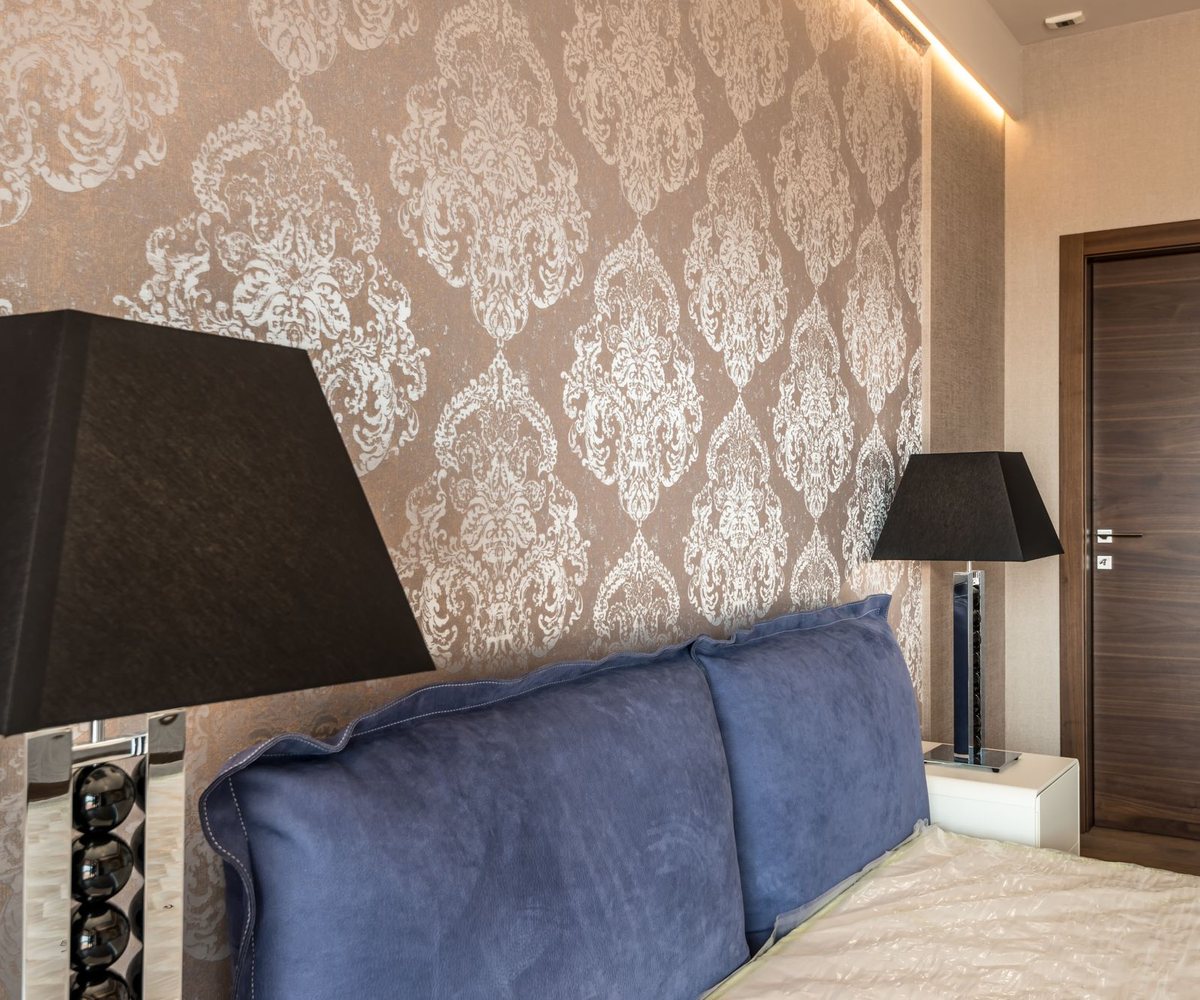 Bedroom with an elegant damask wallpaper wall behind a blue upholstered headboard